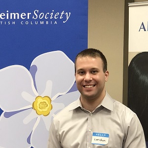 Landon smiling in front of a blue Alzheimer Society of B.C. banner.